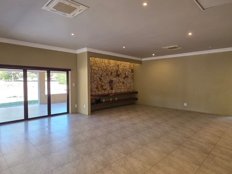 Spacious living area featuring a stone-clad fireplace with a wood-burning stove, tiled flooring, recessed lighting, and large sliding doors leading to the patio.