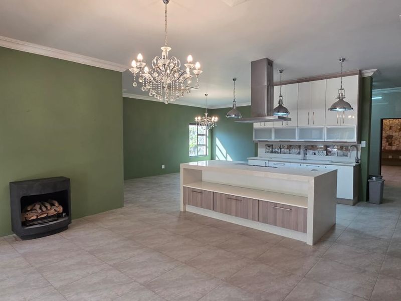 Spacious open-plan living and kitchen area featuring a built-in fireplace, modern kitchen island, and neutral tiled flooring throughout.