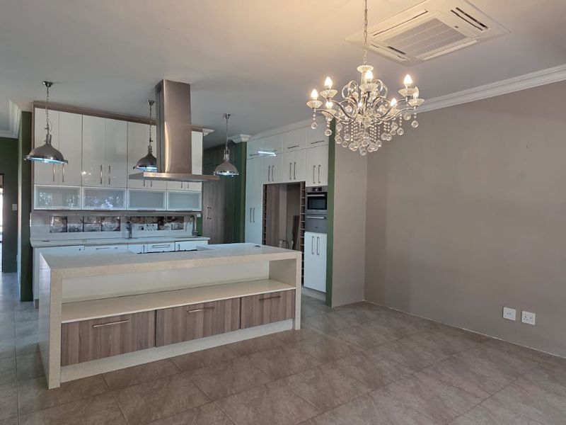 Modern kitchen featuring a central island, sleek built-in cabinetry, integrated appliances, and ducted air conditioning, finished with neutral tones and tiled flooring.