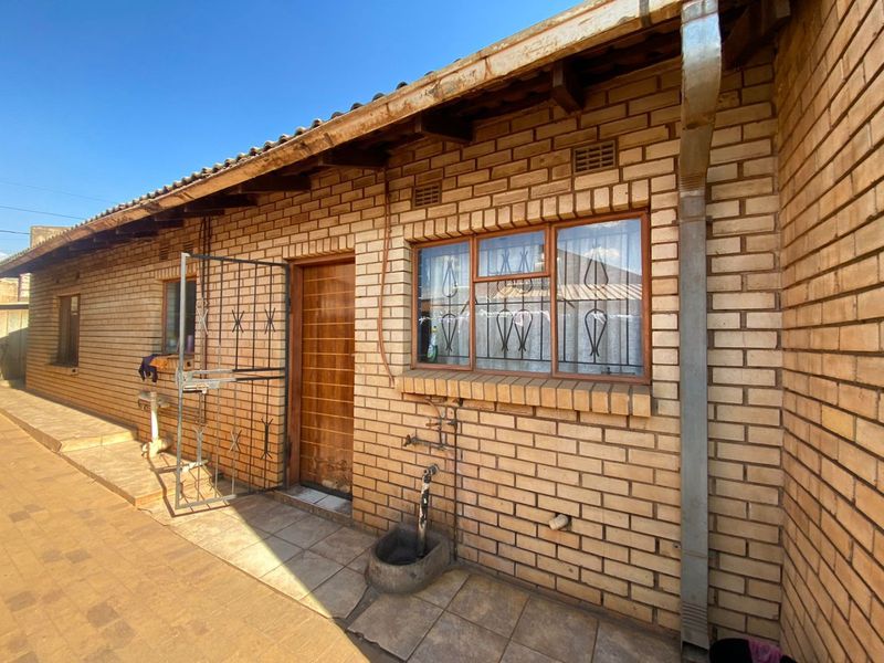 Rear exterior view of a face brick house featuring a tiled patio, security gates, and steel-framed windows with security bars.