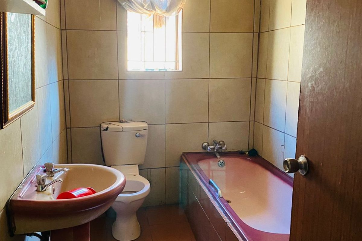 A dated bathroom featuring a pedestal basin, toilet, and built-in bathtub with tiled walls and flooring, requiring modernization.