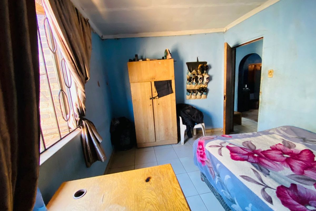 A bedroom featuring tiled flooring and a window with security bars, requiring cosmetic updates to the wall finishes.