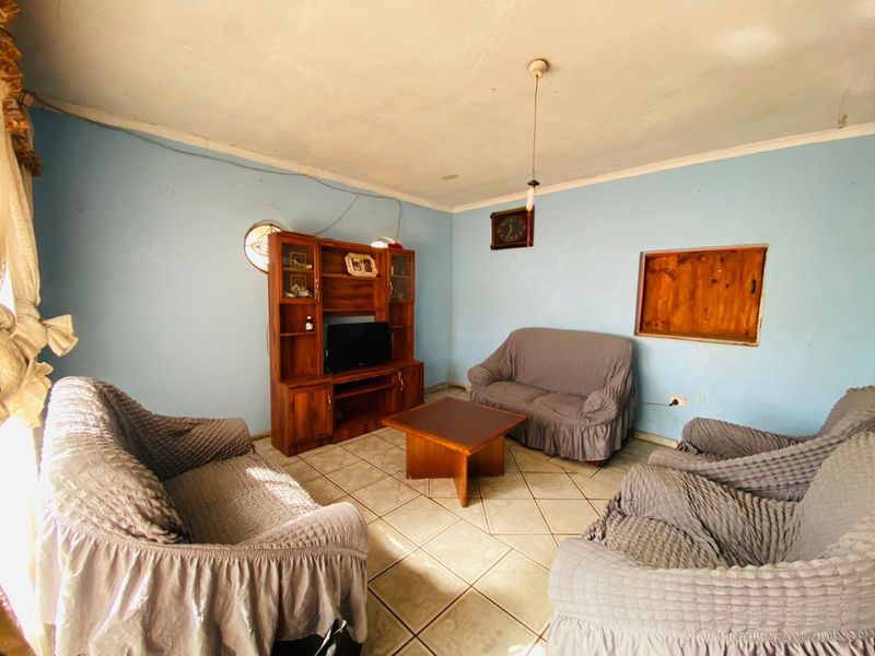 A living room featuring tiled flooring, a circular window, and a rectangular wall opening, requiring cosmetic updates to improve the overall aesthetic.