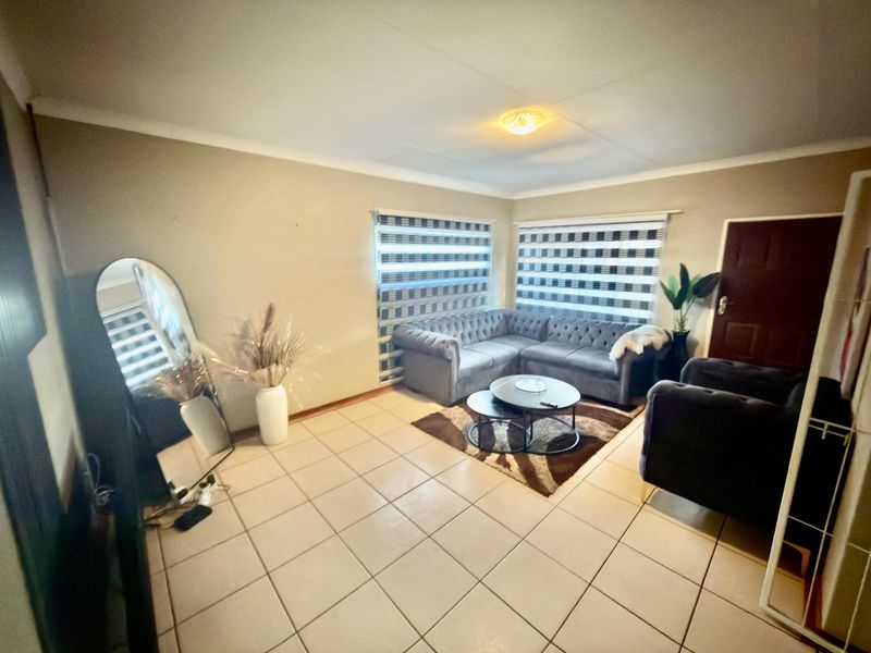 A living room featuring tiled flooring, coved ceilings, and zebra blinds, providing a functional and neutral space for relaxation.