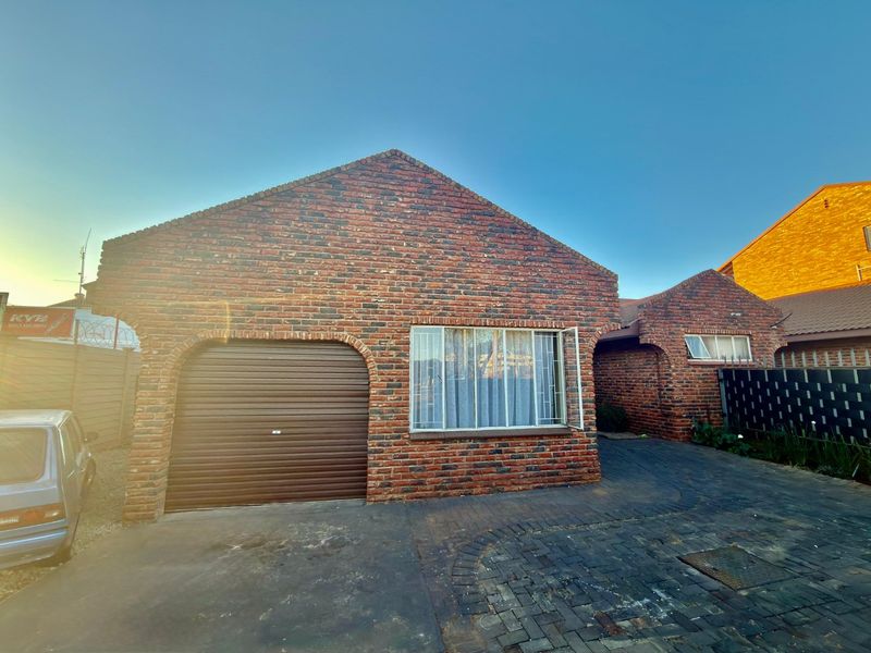 Front elevation of a face brick townhouse featuring a single roller garage door, paved driveway, and security-fitted windows.