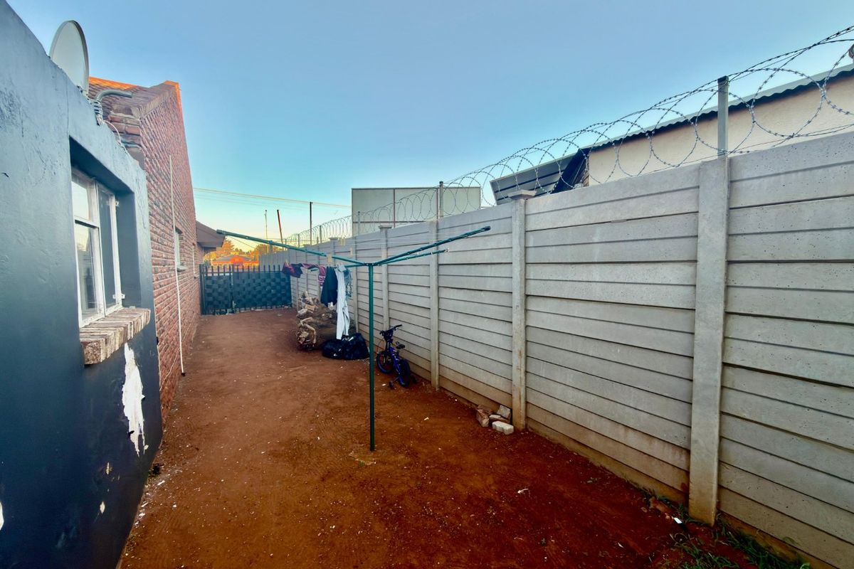 Rear exterior area featuring a precast concrete boundary wall with razor wire security and an unpaved ground surface.