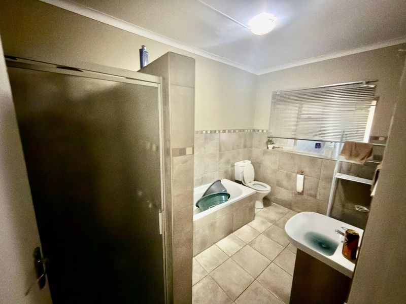 A functional bathroom featuring a shower enclosure, built-in bathtub, toilet, and vanity basin with neutral wall and floor tiling.