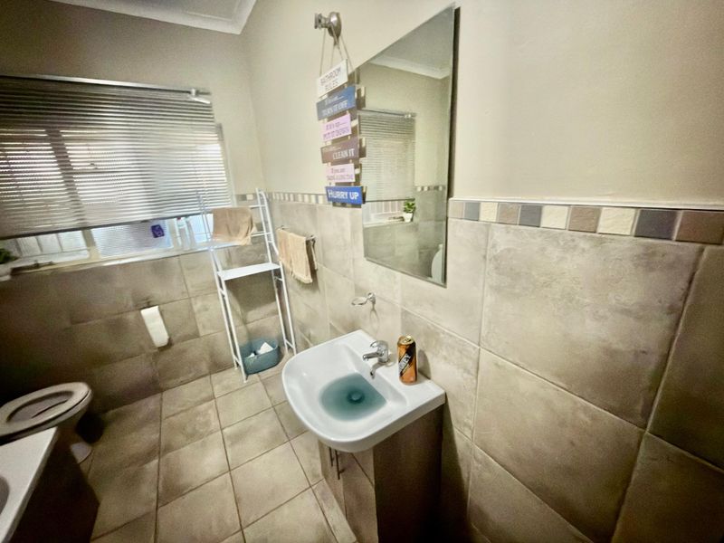A functional bathroom featuring a pedestal basin, wall-mounted mirror, and neutral ceramic tiling throughout.