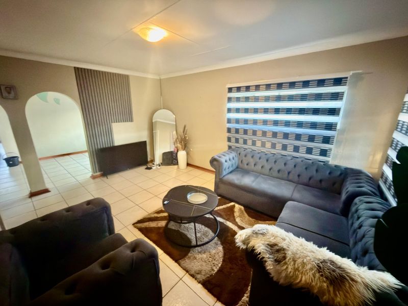 A living room featuring tiled flooring, an arched entryway, and modern roller blinds, providing a functional space with potential for aesthetic updates.