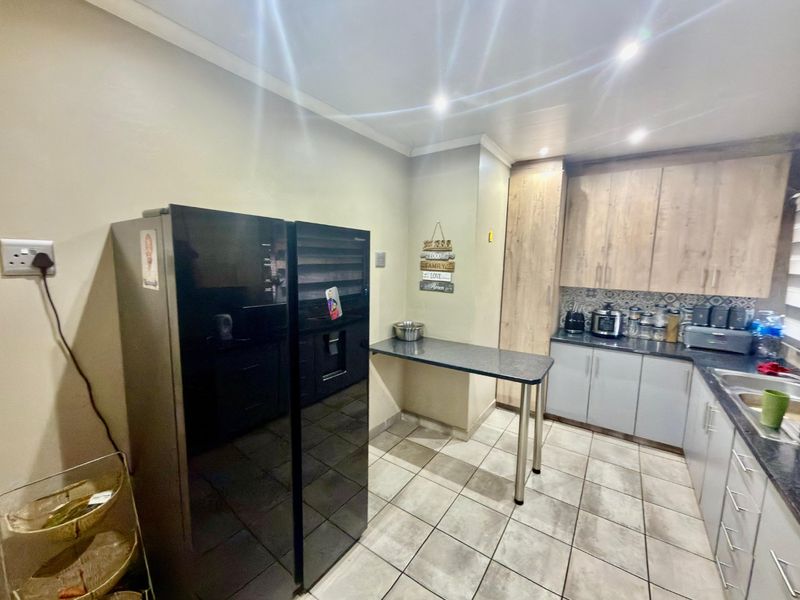 A functional kitchen featuring light wood-tone cabinetry, dark laminate countertops, a patterned tile backsplash, and tiled flooring with integrated lighting.
