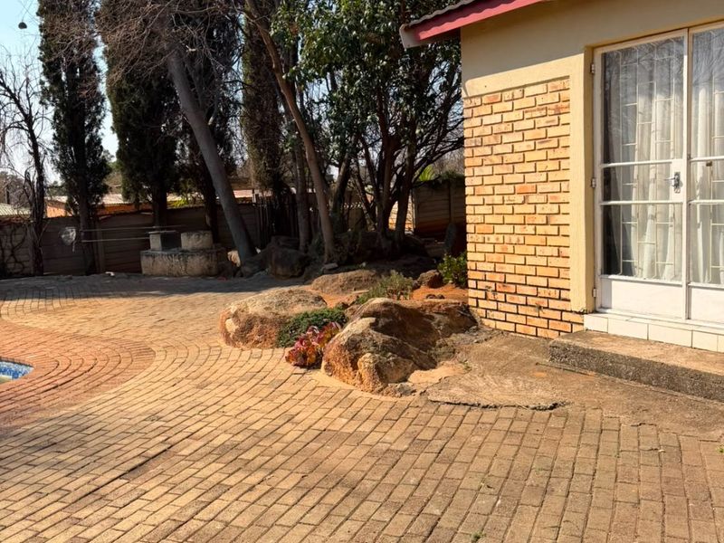 Rear exterior view featuring a brick-paved patio area, swimming pool, and access to the home via a glass sliding door.