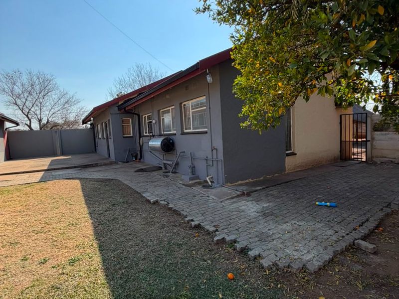 Rear exterior view of the house featuring a paved patio area, lawn, solar water heater, and secure boundary walling.