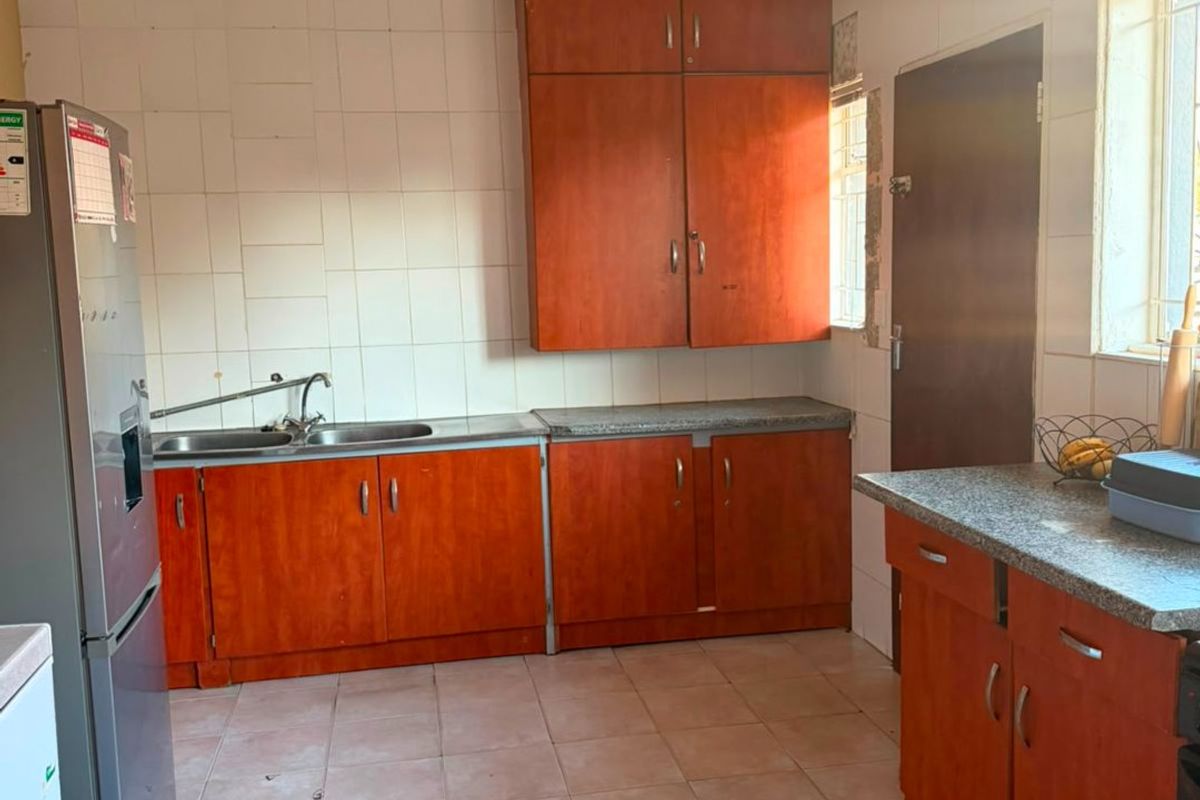 A functional kitchen featuring wooden cabinetry, laminate countertops, a stainless steel double sink, and tiled flooring with a neutral splashback.