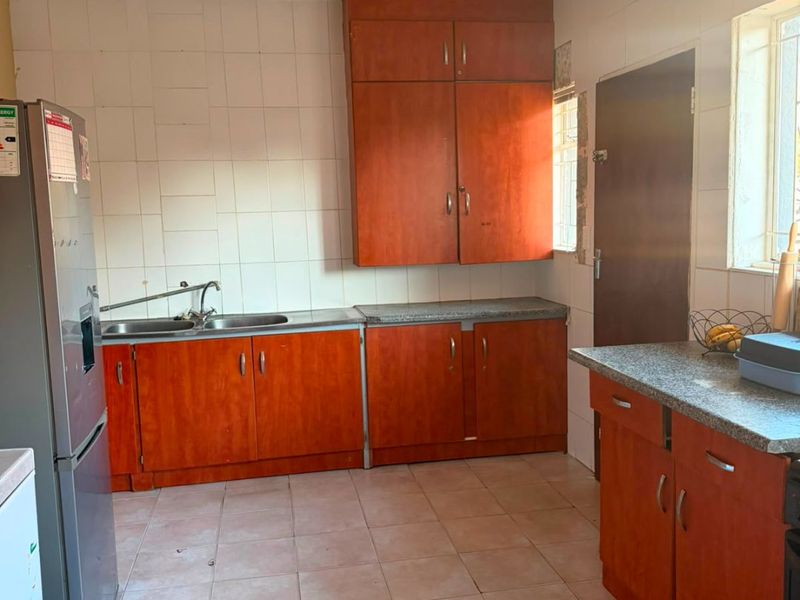 A functional kitchen featuring wooden cabinetry, laminate countertops, a stainless steel double sink, and tiled flooring with a neutral splashback.