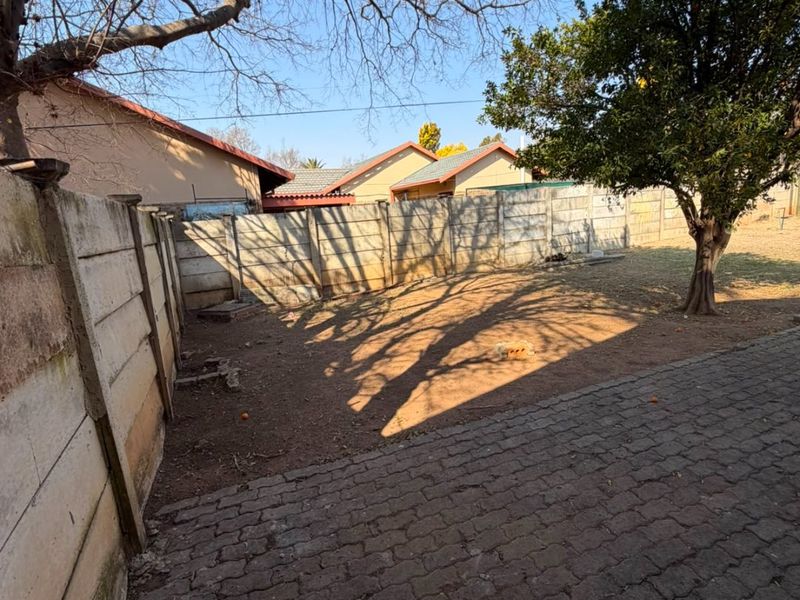 A rear garden area featuring a paved section, mature trees, and a precast concrete boundary wall, offering potential for landscaping and outdoor improvement.