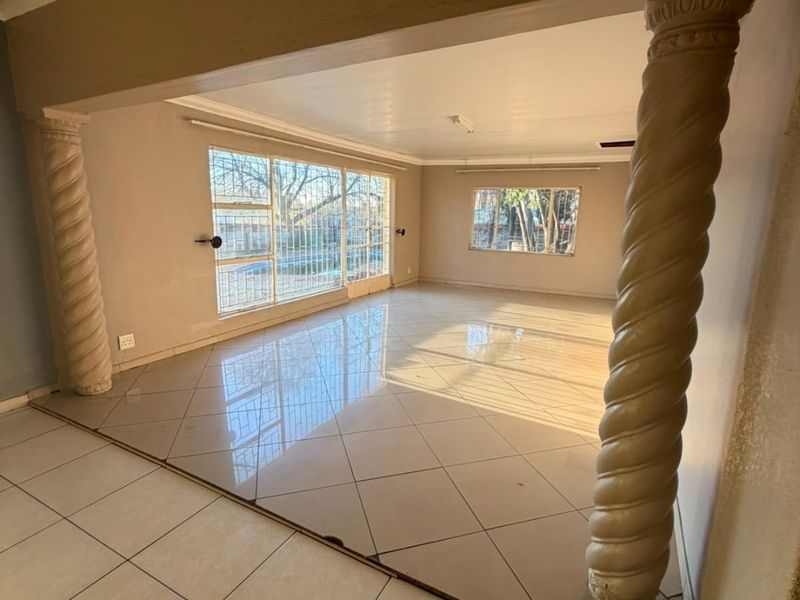 Spacious, empty living area featuring decorative columns, large windows with security bars, and neutral tiled flooring throughout.