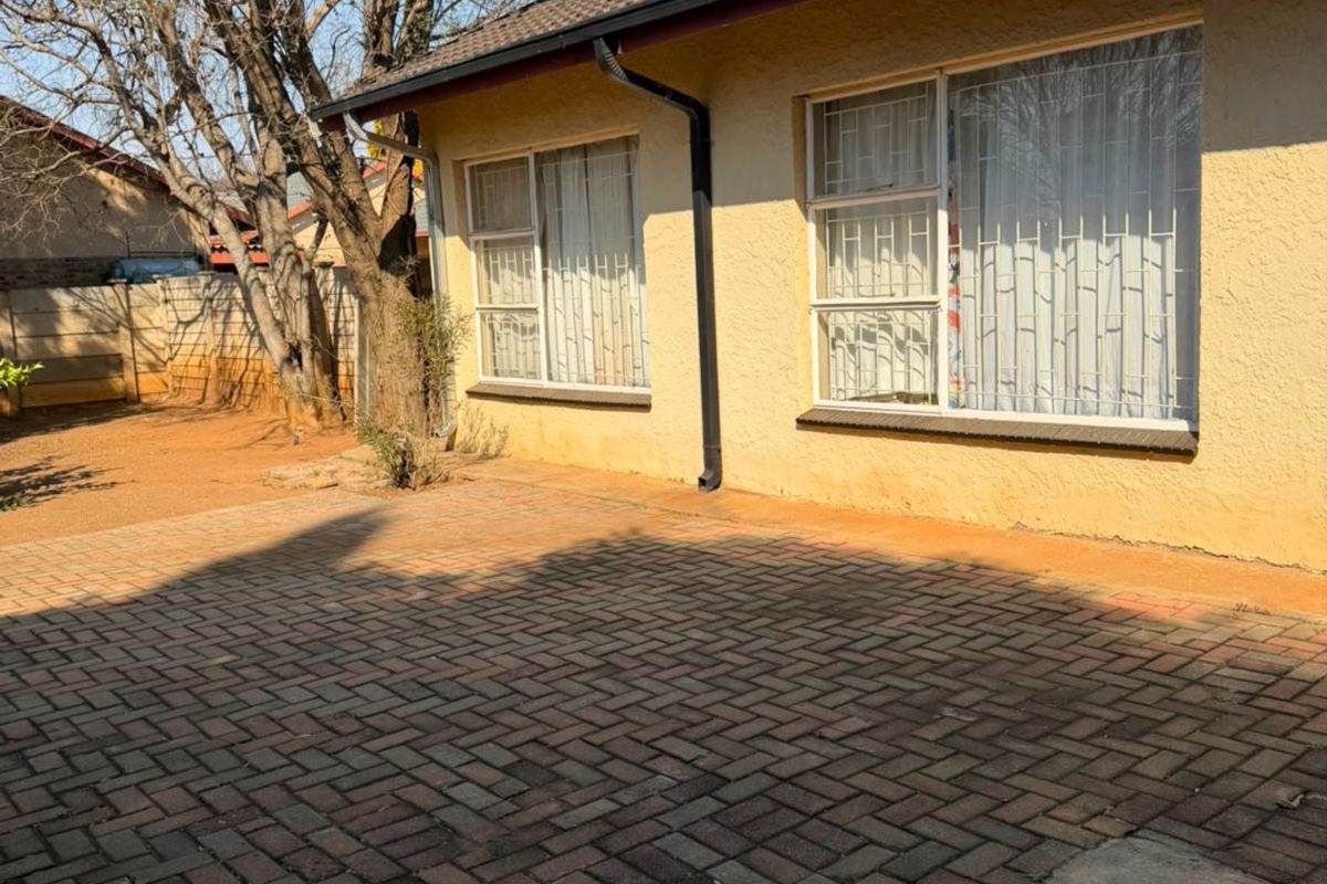 Rear exterior view of the house featuring a paved patio area, tiled roof, and security bars on the windows.