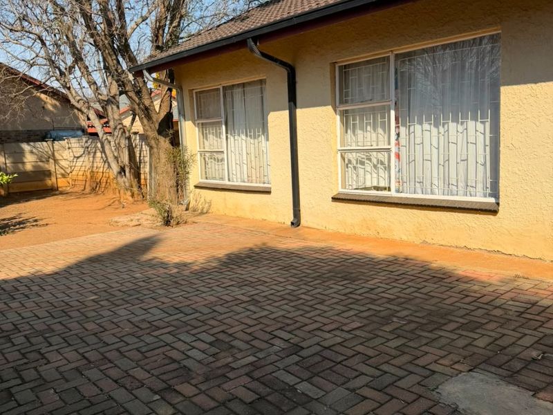 Rear exterior view of the house featuring a paved patio area, tiled roof, and security bars on the windows.