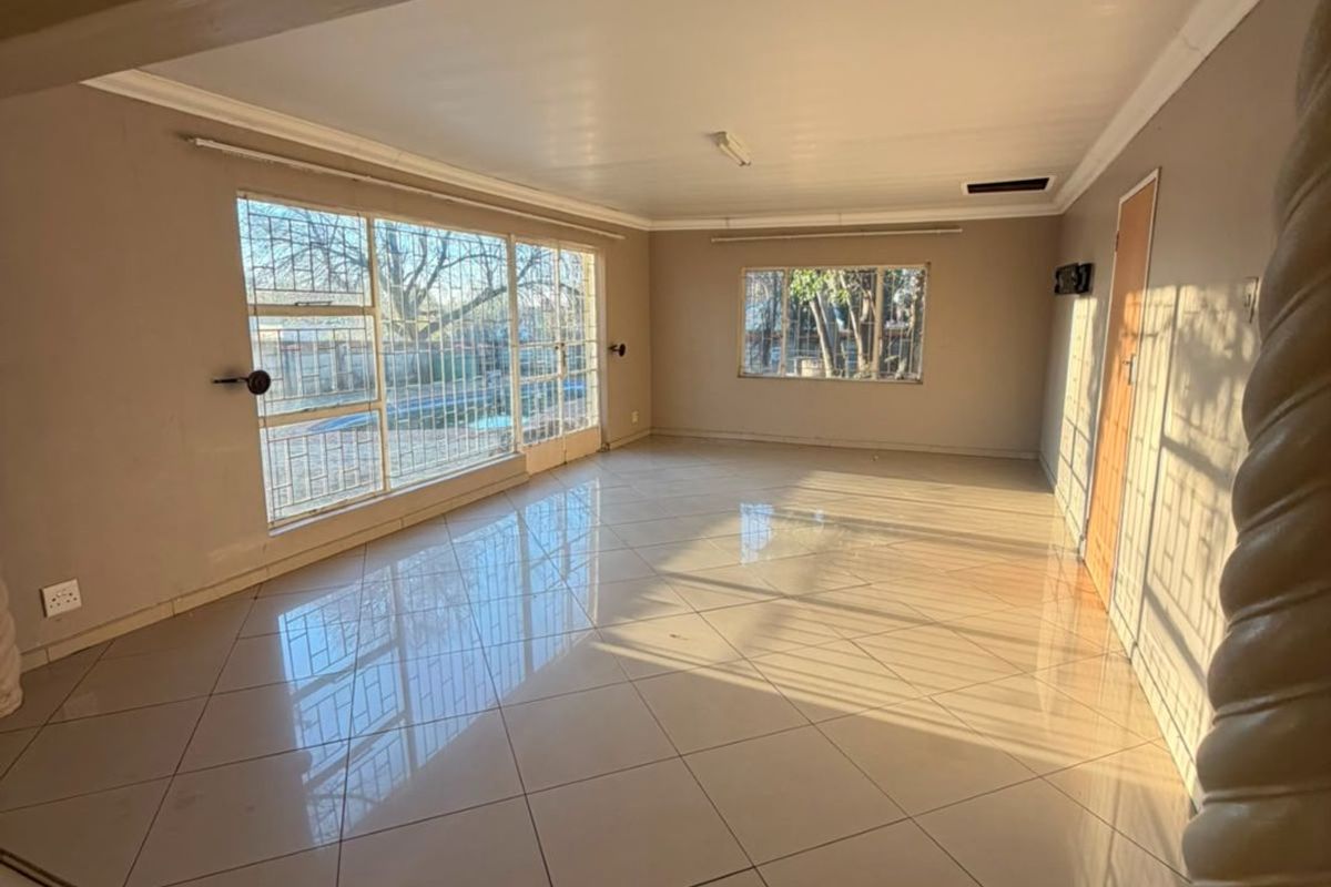 A spacious, empty living area featuring large windows, polished tiled flooring, and a decorative pillar, offering a bright and versatile blank canvas.