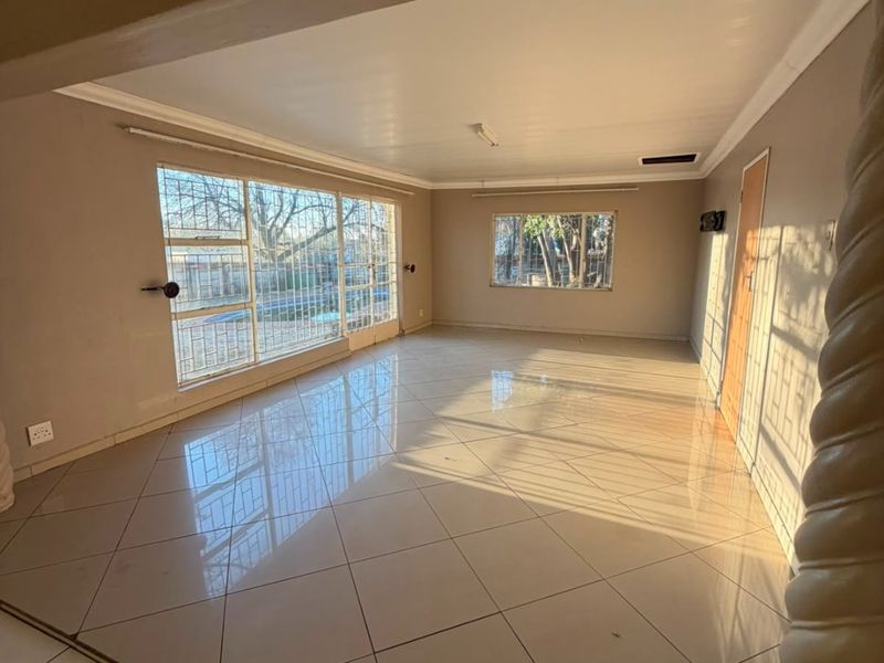 A spacious, empty living area featuring large windows, polished tiled flooring, and a decorative pillar, offering a bright and versatile blank canvas.