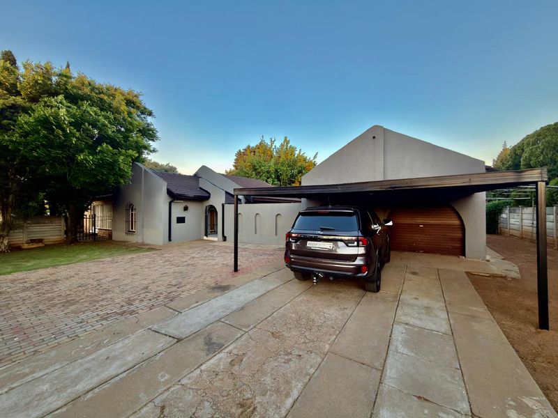 Front exterior view of the house featuring a brick and concrete driveway, a covered carport, and a garage with a wooden door.