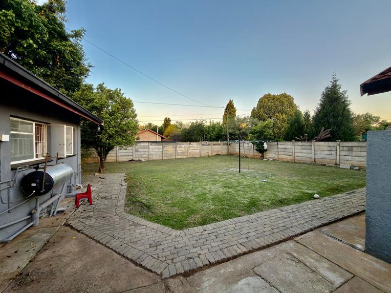 A spacious rear garden featuring a lawn, paved perimeter walkway, and a precast concrete boundary wall, providing a private outdoor area.