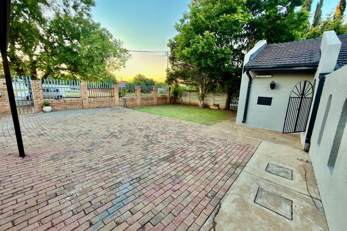 A spacious rear exterior area featuring brick paving, a small lawn, and secure perimeter walling with metal fencing.