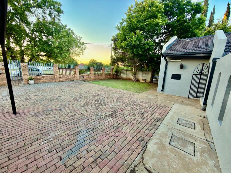 A spacious rear exterior area featuring brick paving, a small lawn, and secure perimeter walling with metal fencing.