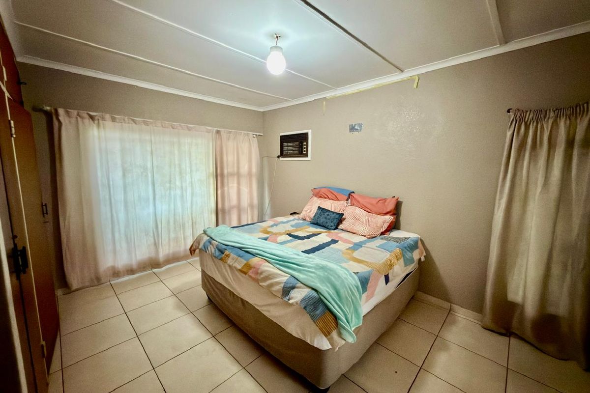 A bedroom featuring tiled flooring, a built-in cupboard, and a wall-mounted air conditioning unit. The room requires cosmetic attention to wall finishes.