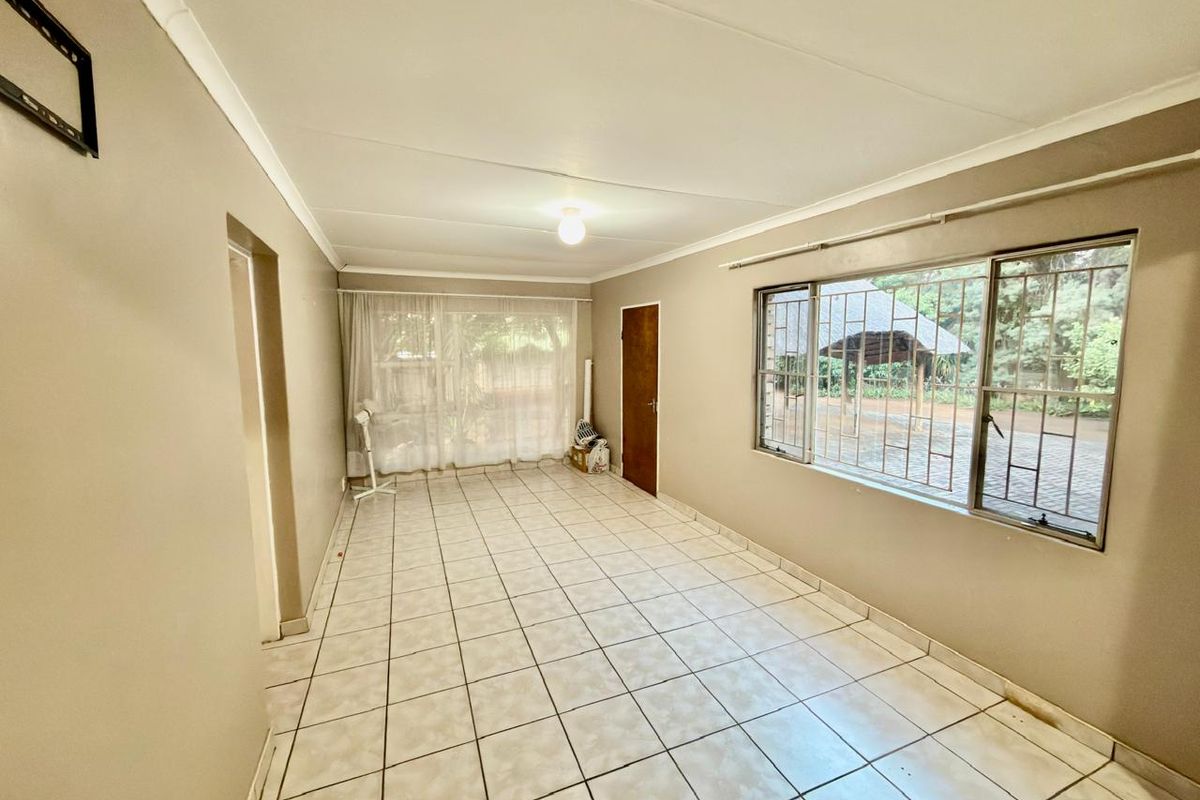 An empty living room featuring tiled flooring, security bars on windows, and a sliding door leading to the exterior.