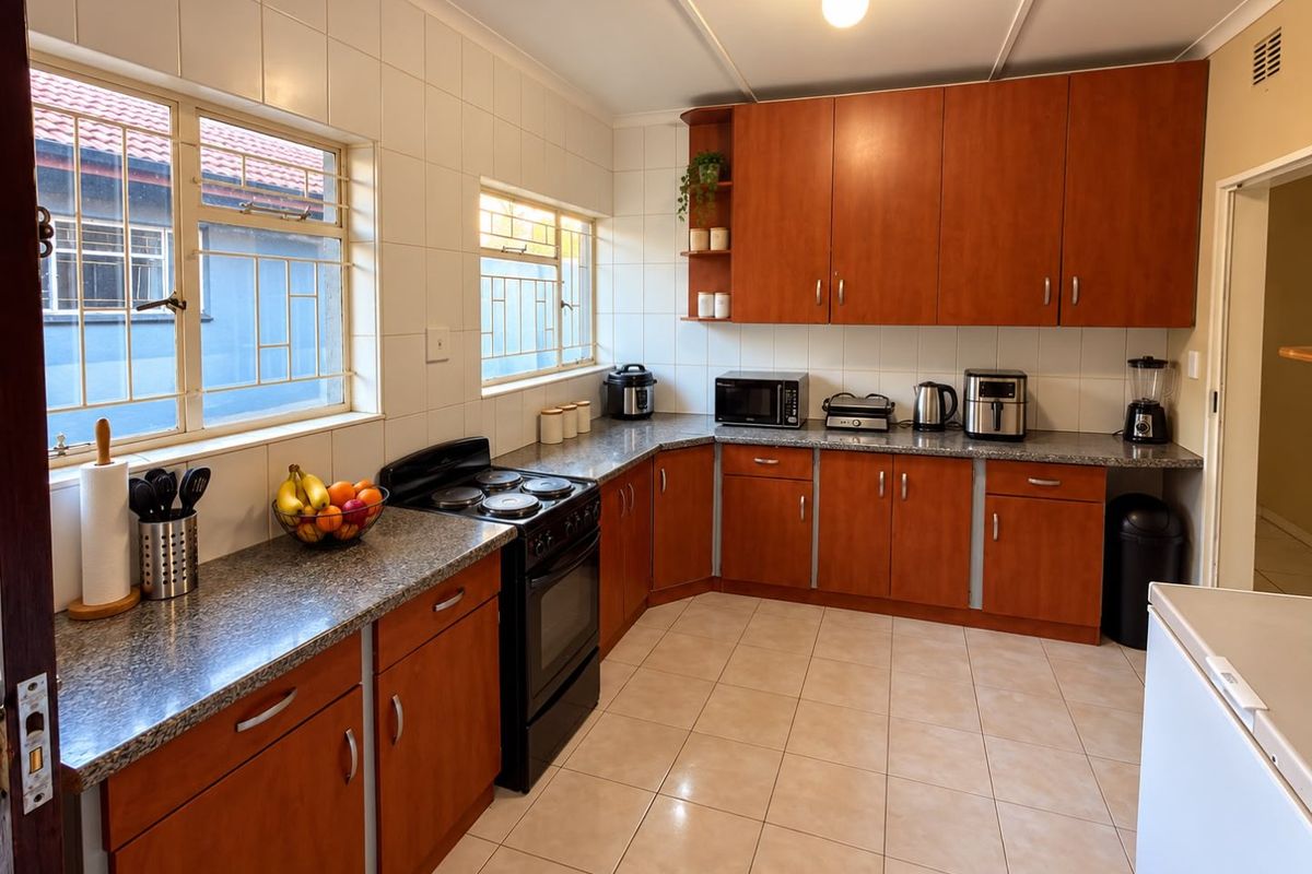 A functional kitchen featuring wood-finish cabinetry, granite countertops, tiled backsplash, and a freestanding electric stove with security-barred windows.