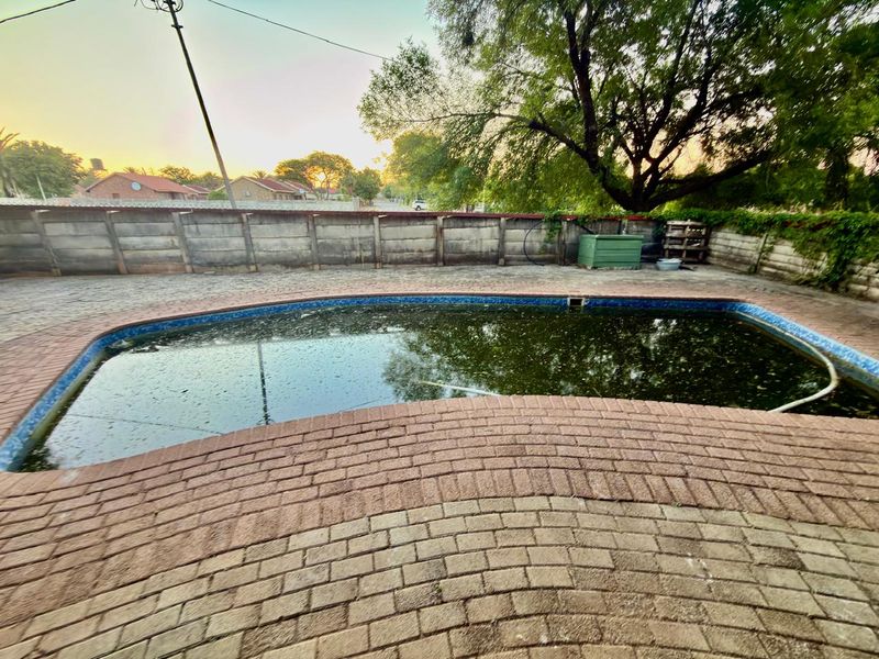 Outdoor pool area featuring brick paving and a perimeter precast concrete wall, currently requiring significant maintenance and water treatment.