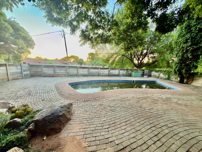 Outdoor pool area featuring a paved deck and precast boundary wall, currently requiring significant maintenance and pool restoration.