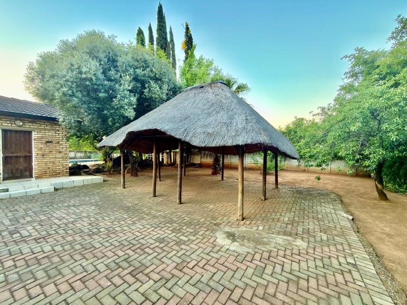 Outdoor entertainment area featuring a traditional thatch roof lapa set over brick paving, providing a shaded space within the garden.