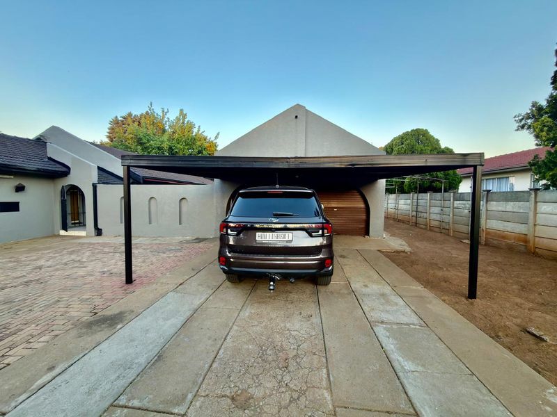 Front exterior view featuring a modern black steel carport, paved driveway, and a secure garage entrance with a roll-up door.