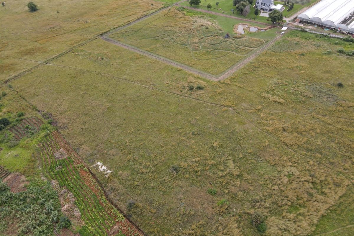 An aerial view of a large, open residential vacant land plot featuring natural grassland, perimeter fencing, and a small pond.