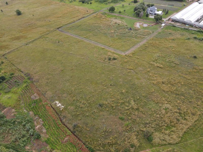 An aerial view of a large, open residential vacant land plot featuring natural grassland, perimeter fencing, and a small pond.
