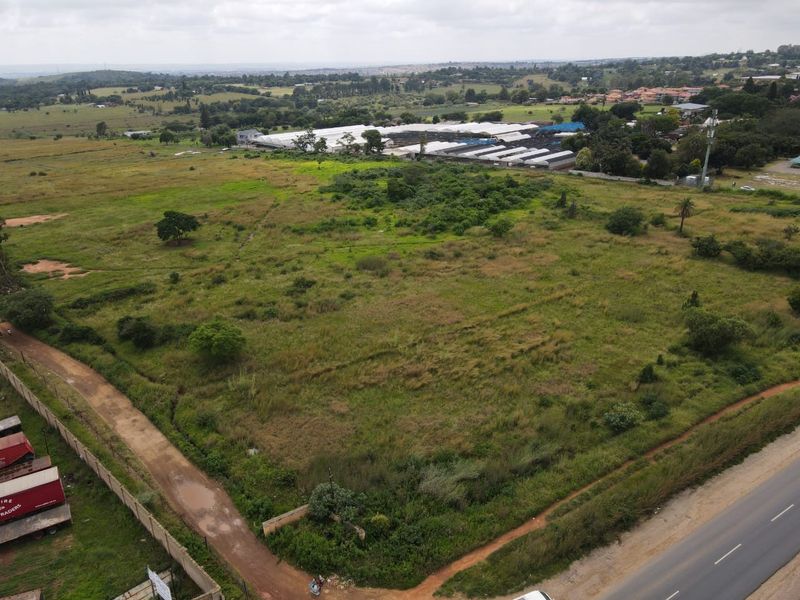 An aerial view of a large, undeveloped residential plot featuring natural vegetation, perimeter fencing, and direct access to a nearby road.