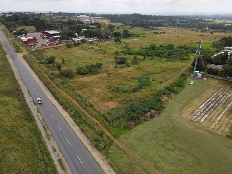 Aerial view of a large vacant residential plot adjacent to a main road, featuring natural vegetation and an existing telecommunications tower.