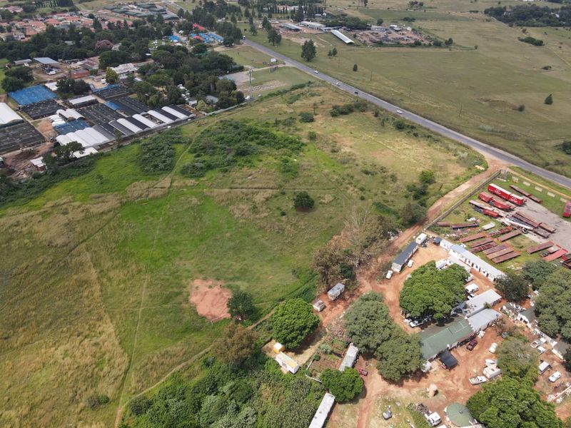 An aerial view of a large, undeveloped residential land parcel situated near a main road and existing commercial or industrial structures.