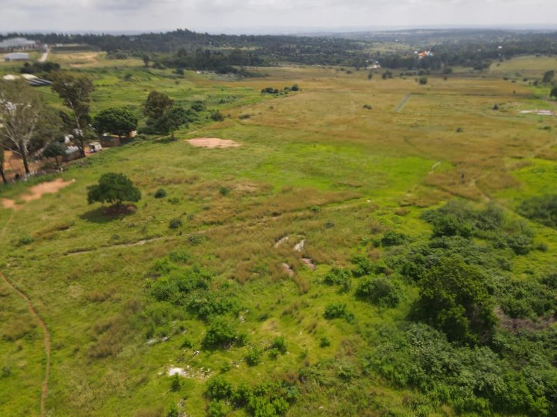 An aerial view of a large, undeveloped residential land plot featuring natural vegetation and surrounding landscape.