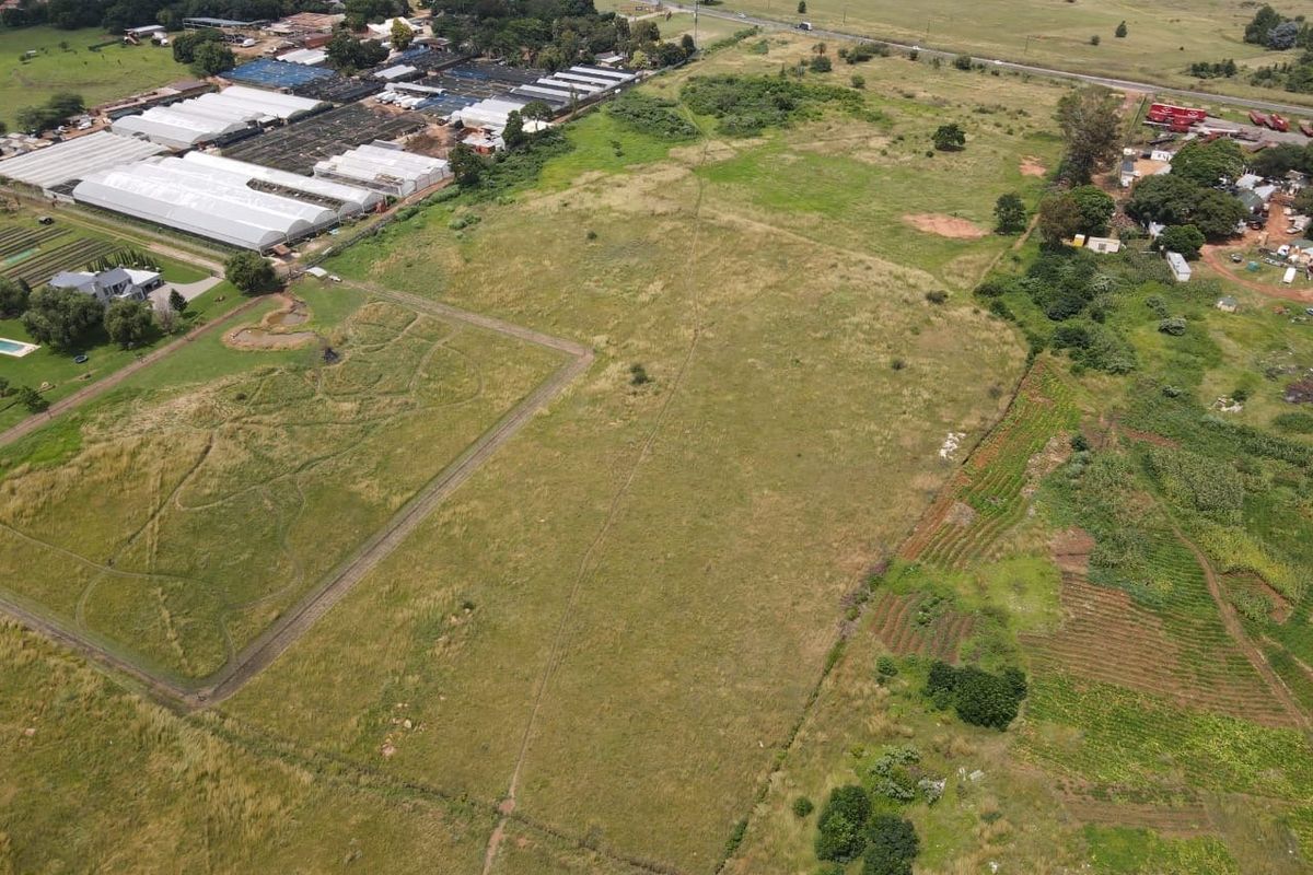 An aerial view of a large, undeveloped residential plot of land featuring open grassland and surrounding rural landscape.