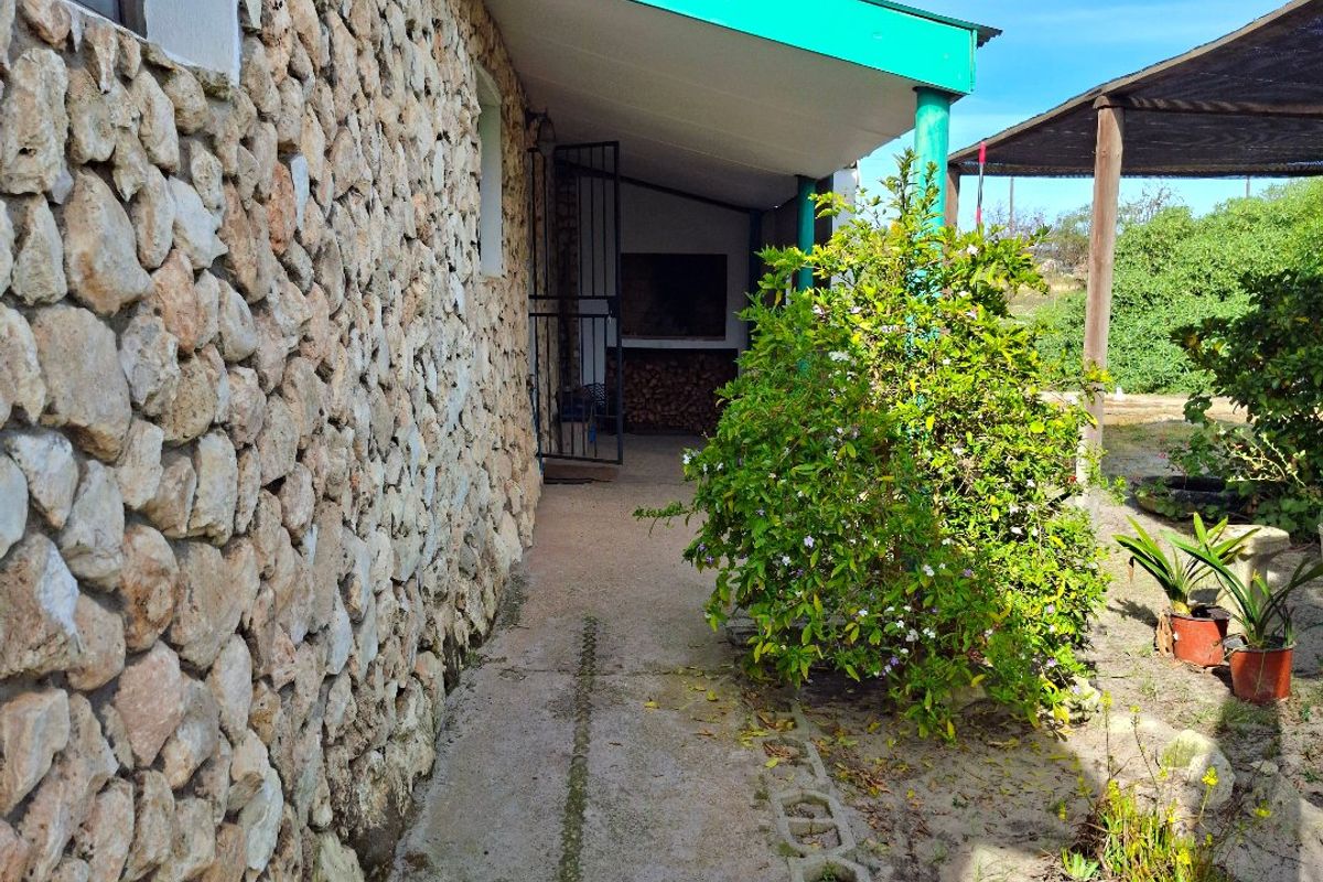 Rear exterior view featuring a stone-clad wall, a covered walkway with a metal roof, and a concrete pathway leading along the side of the house.