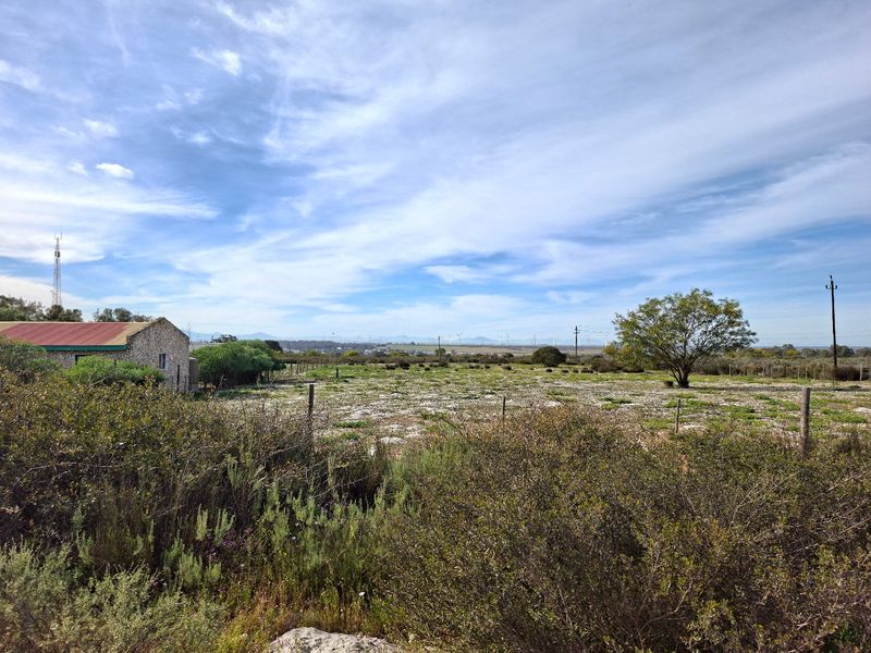 A wide-angle view of the property grounds featuring a stone building with a metal roof and expansive open landscape.