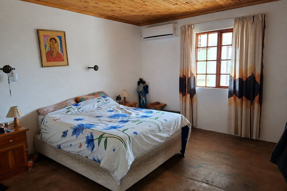 A bedroom featuring a timber-paneled ceiling, split-system air conditioning, and a timber-framed window, with concrete flooring throughout.