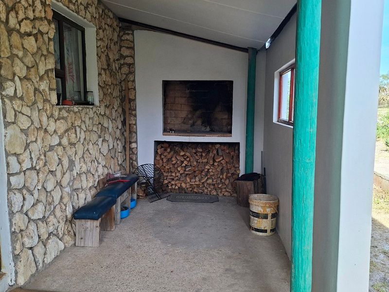 A covered outdoor patio area featuring stone cladding, a built-in braai, and timber support posts, providing a functional space for outdoor entertaining.