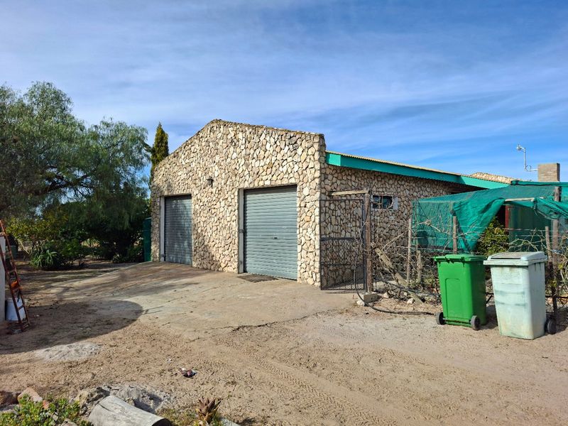 A detached garage building featuring stone cladding and two roller doors, situated on a concrete driveway.