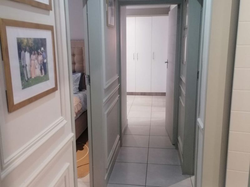 A well-maintained hallway featuring decorative wainscoting, neutral tiled flooring, and access to adjacent bedrooms with built-in storage.