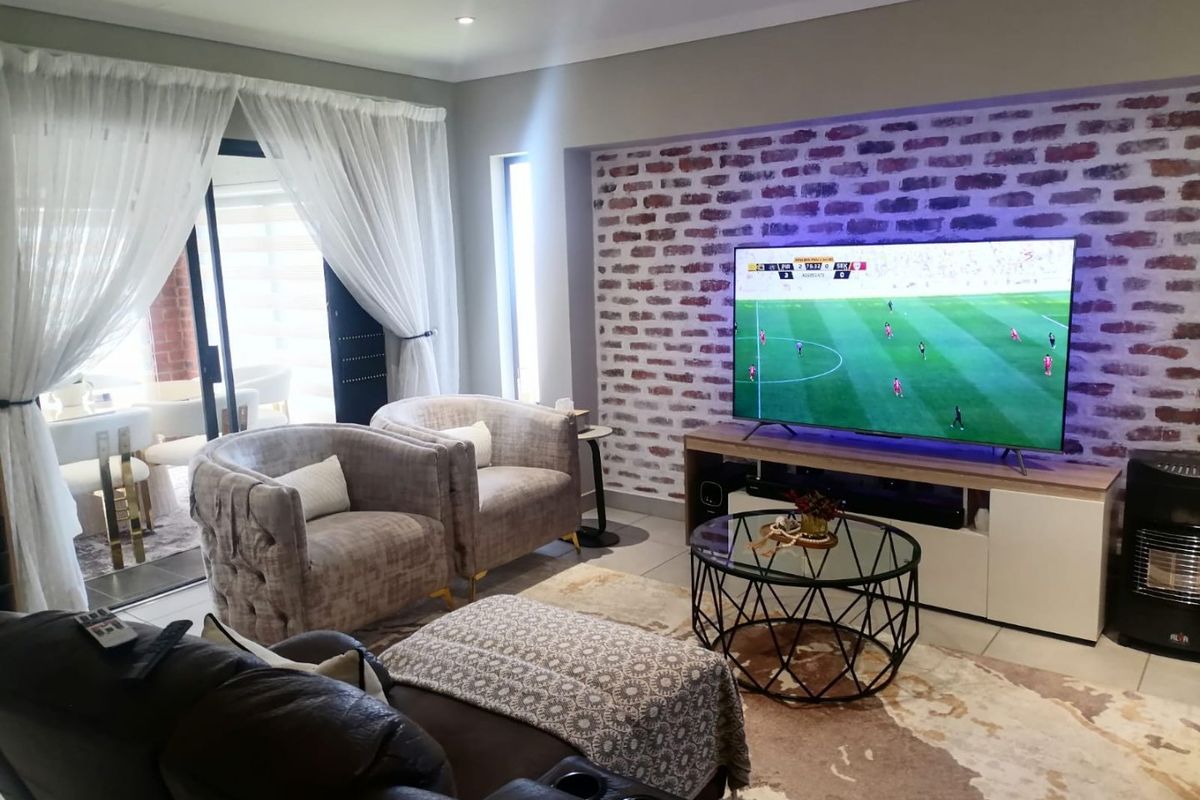 A comfortable living room featuring an exposed brick accent wall, tiled flooring, and large sliding glass doors providing access to the patio.