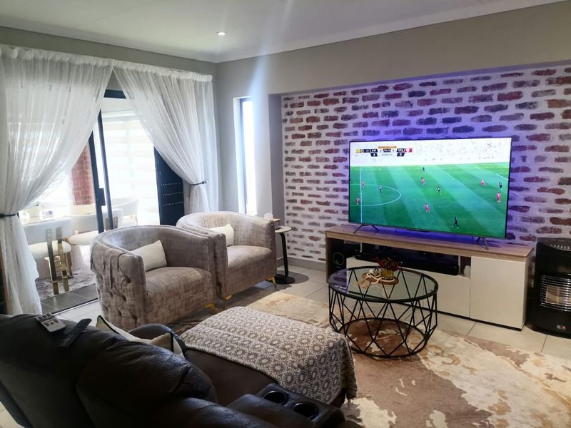 A comfortable living room featuring an exposed brick accent wall, tiled flooring, and large sliding glass doors providing access to the patio.